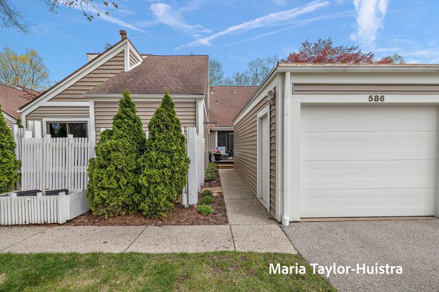 view of side of home featuring roof with shingles, fence, and a garage