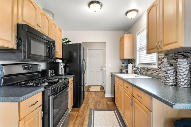 kitchen with light brown cabinetry, tasteful backsplash, a sink, black appliances, and light wood-style floors