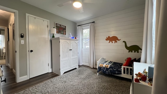 bedroom with dark wood-type flooring, wood walls, and ceiling fan