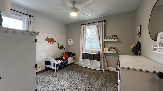bedroom featuring a crib, baseboards, wood walls, and ceiling fan