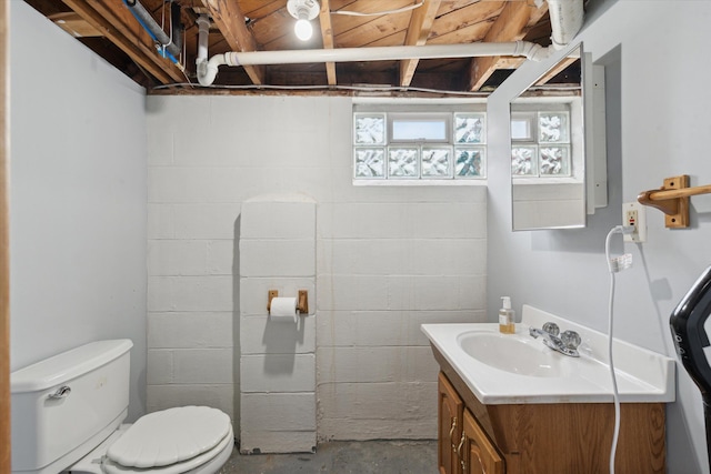 half bathroom with vanity, concrete block wall, toilet, and unfinished concrete floors