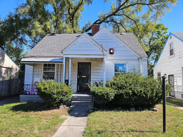 bungalow featuring a porch, a front yard, a chimney, and roof with shingles