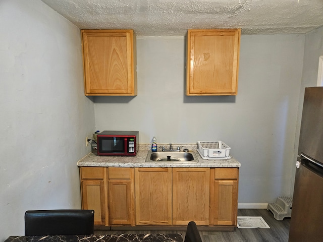 kitchen featuring a sink, light countertops, a textured ceiling, freestanding refrigerator, and dark wood-style floors