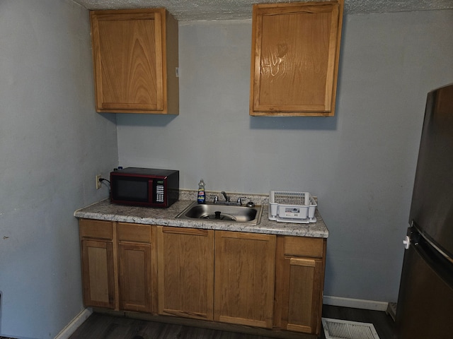kitchen featuring a sink, baseboards, freestanding refrigerator, and brown cabinetry