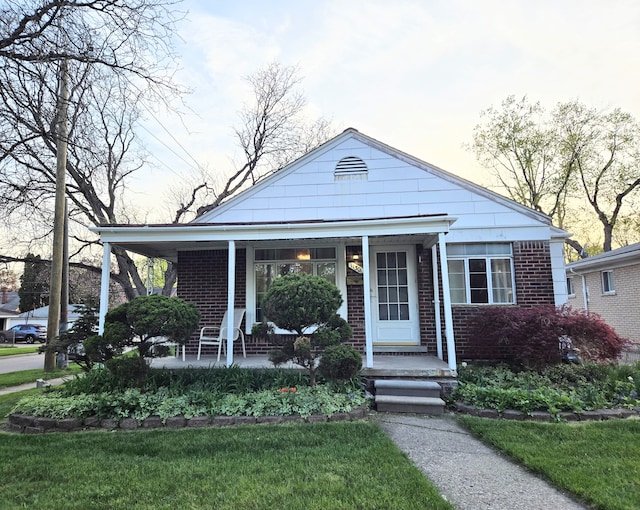 view of front of home featuring brick siding, a front lawn, and a porch