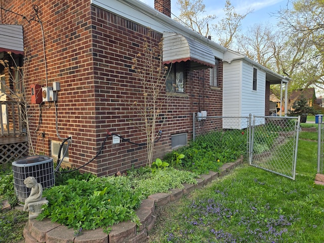 view of property exterior featuring a chimney, a gate, brick siding, central AC, and fence