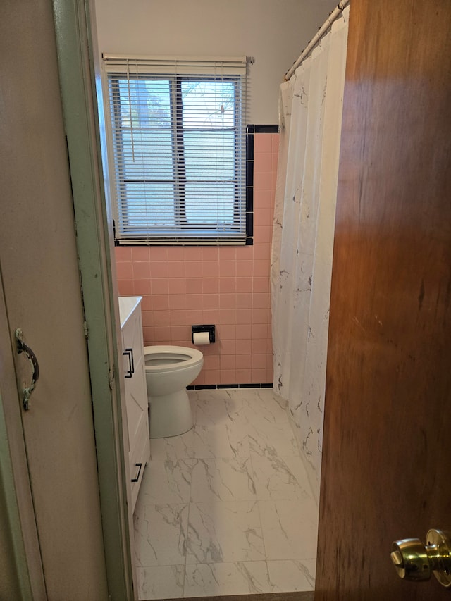 bathroom with vanity, toilet, marble finish floor, tile walls, and curtained shower