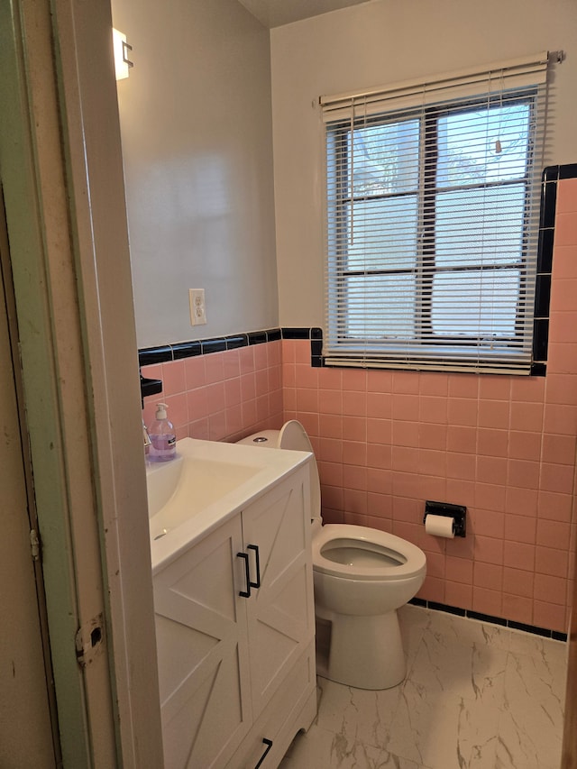 bathroom with toilet, tile walls, a wealth of natural light, and vanity