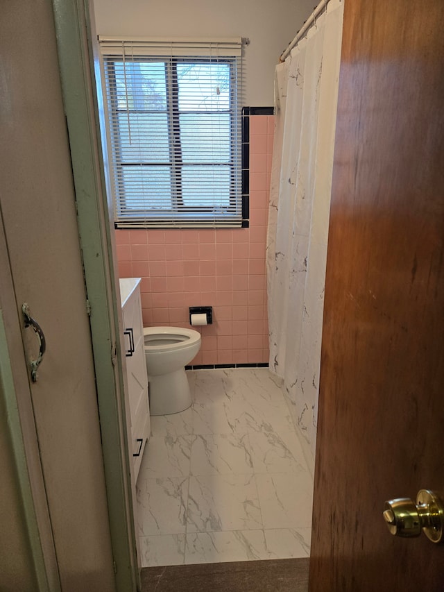 bathroom with vanity, toilet, a shower with shower curtain, marble finish floor, and tile walls