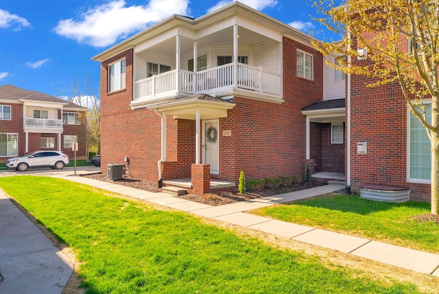 view of front of home with central AC unit, brick siding, a front lawn, and a balcony