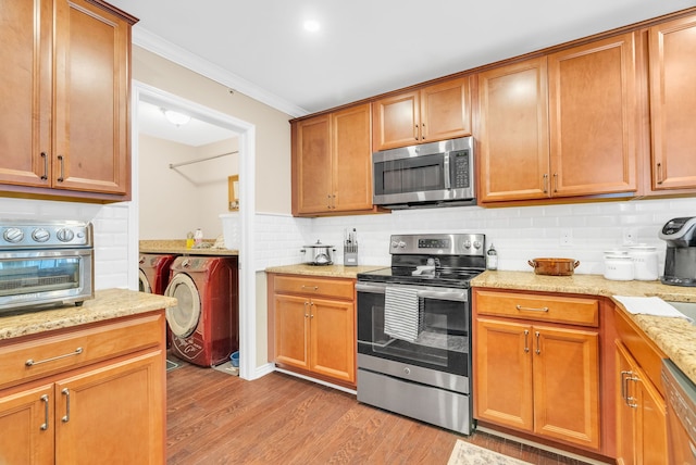 kitchen with decorative backsplash, crown molding, light wood finished floors, stainless steel appliances, and washer and clothes dryer