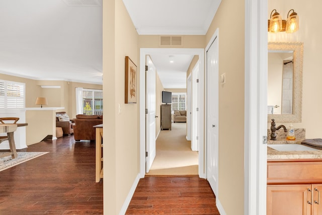 hall with visible vents, crown molding, baseboards, dark wood-style floors, and a sink