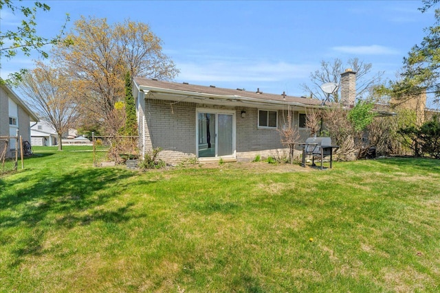 back of property with brick siding, a lawn, and a chimney