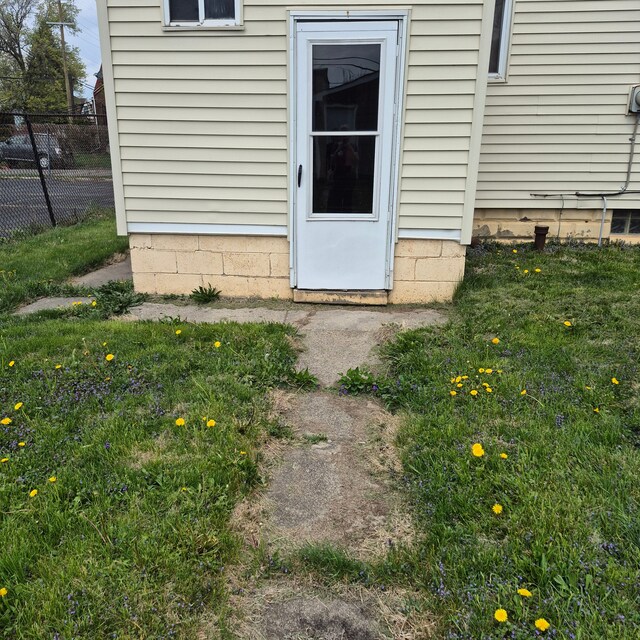 view of exterior entry featuring fence and a lawn