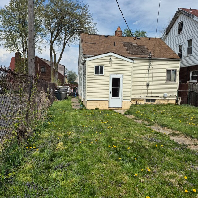 rear view of property featuring a fenced backyard, a chimney, a lawn, and roof with shingles