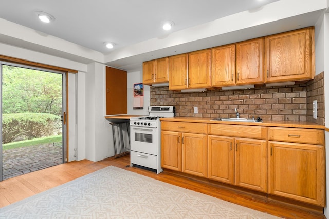 kitchen with a sink, light wood-style flooring, white gas range, and light countertops