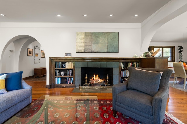 living room featuring arched walkways, recessed lighting, wood finished floors, and a tile fireplace