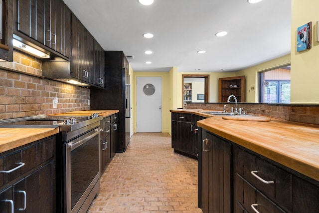 kitchen with a sink, butcher block counters, brick floor, and stainless steel electric range oven