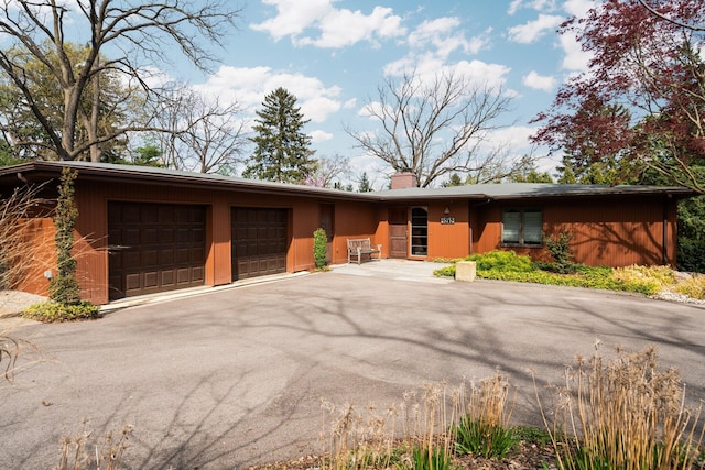 view of front of home featuring an attached garage, a chimney, and aphalt driveway