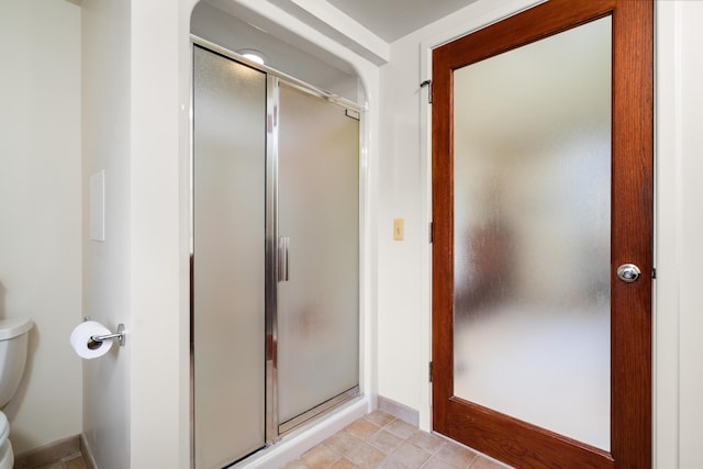 bathroom featuring toilet, baseboards, and a stall shower