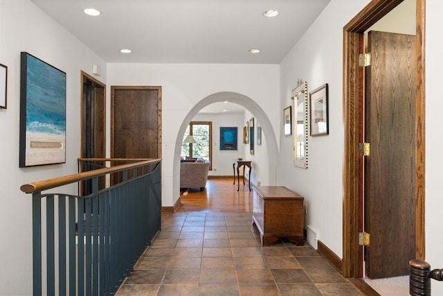 hallway with dark tile patterned flooring, arched walkways, baseboards, and recessed lighting