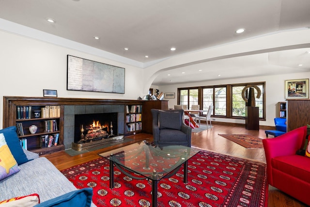 living area featuring recessed lighting, arched walkways, wood finished floors, and a tile fireplace