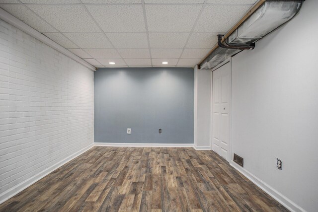 finished basement with baseboards, wood finished floors, brick wall, and visible vents