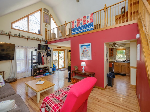 living area with high vaulted ceiling, plenty of natural light, a ceiling fan, and light wood-type flooring