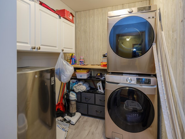 laundry room featuring cabinet space, stacked washing maching and dryer, and light wood finished floors