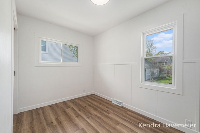 spare room with plenty of natural light, a decorative wall, dark wood finished floors, and visible vents