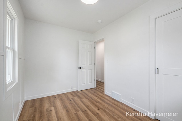 unfurnished bedroom with baseboards, visible vents, multiple windows, and wood finished floors