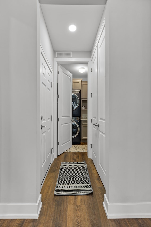 corridor with baseboards, visible vents, dark wood-style floors, and stacked washer and clothes dryer