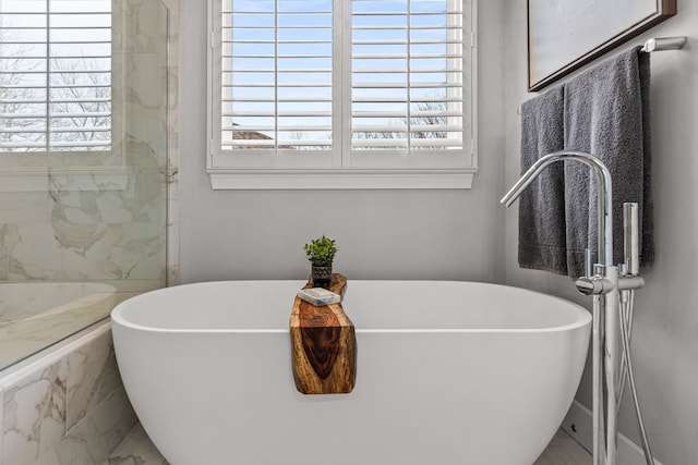 bathroom featuring marble finish floor, a healthy amount of sunlight, and a soaking tub