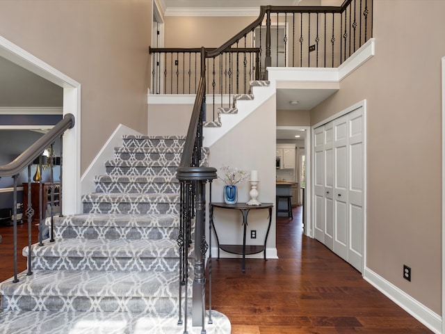stairway featuring crown molding, baseboards, wood finished floors, and a towering ceiling
