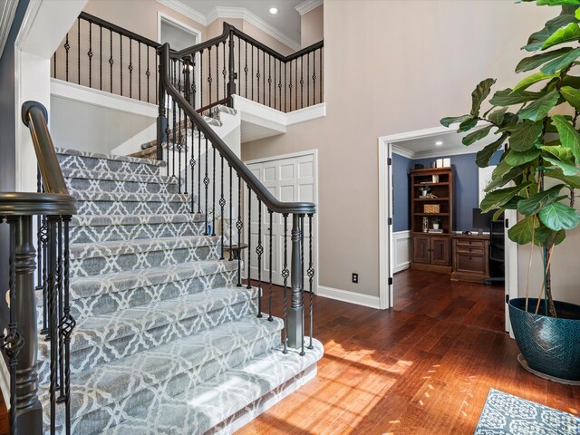 stairs featuring a towering ceiling, wood finished floors, baseboards, ornamental molding, and recessed lighting