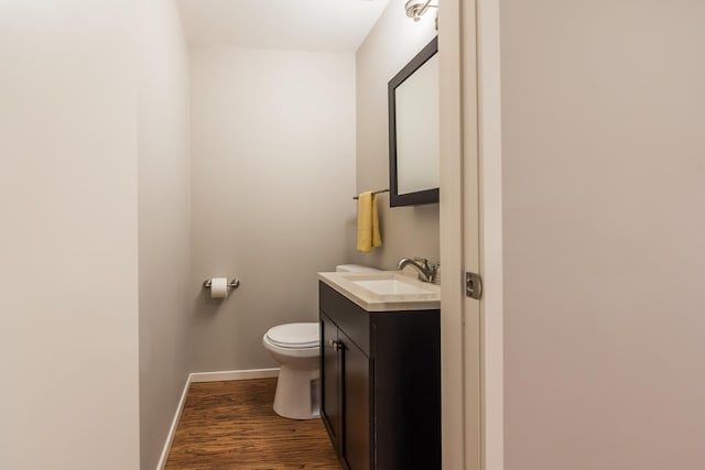 half bathroom with toilet, baseboards, wood finished floors, and vanity