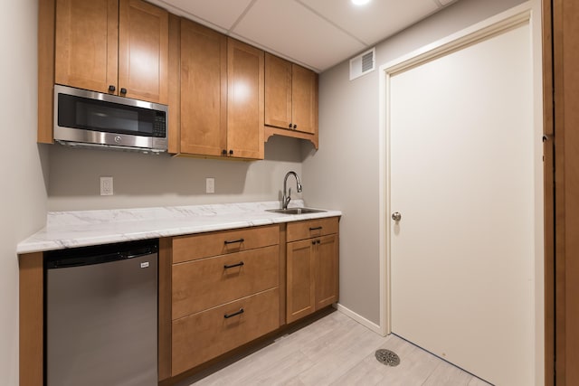 kitchen with visible vents, brown cabinetry, fridge, stainless steel microwave, and a sink