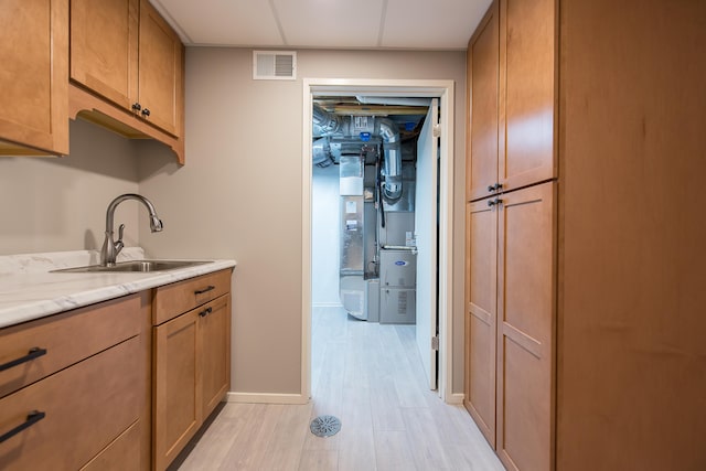 kitchen with visible vents, brown cabinetry, baseboards, a sink, and light wood-style flooring