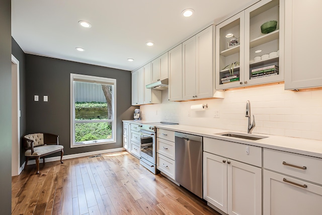 kitchen featuring a sink, stainless steel appliances, backsplash, under cabinet range hood, and glass insert cabinets