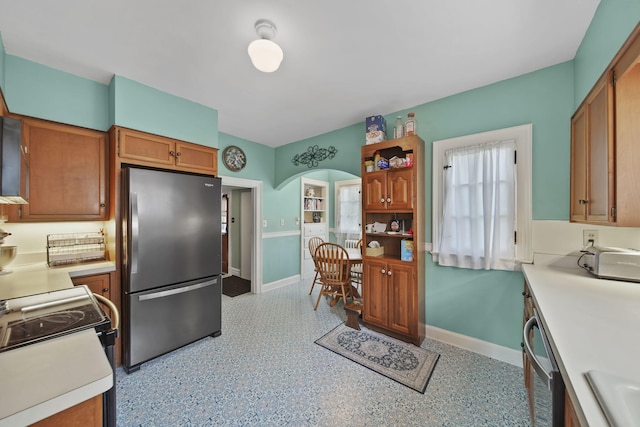 206 S Webster St, Jackson, MI 49203 - kitchen with brown cabinetry, baseboards, light countertops, arched walkways, and appliances with stainless steel finishes