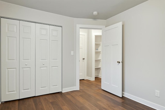 unfurnished bedroom featuring baseboards, a closet, and dark wood-style flooring