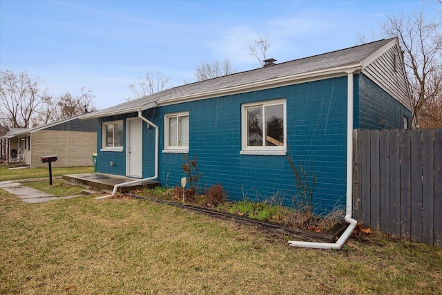 view of front of house featuring brick siding, a shingled roof, a front lawn, and fence
