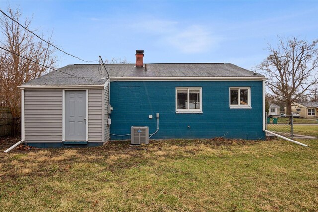 rear view of house featuring central AC unit, fence, a yard, and a chimney