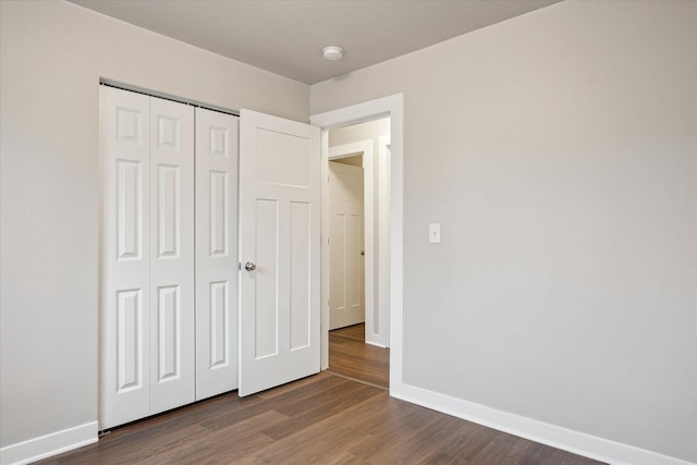 unfurnished bedroom featuring baseboards, wood finished floors, and a closet