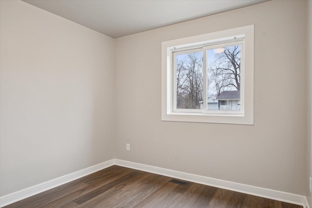 empty room featuring dark wood-style flooring, baseboards, and visible vents