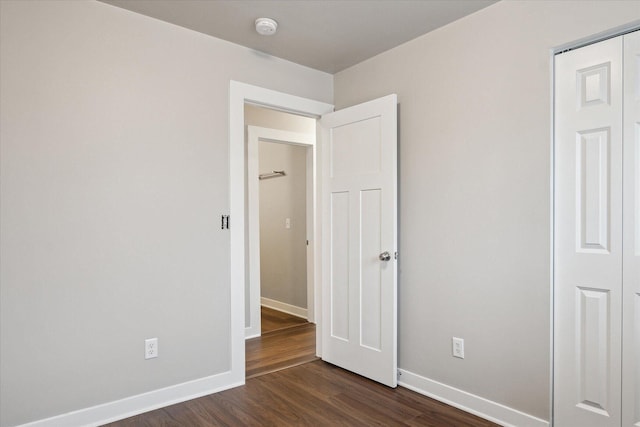 unfurnished bedroom with baseboards, a closet, and dark wood finished floors