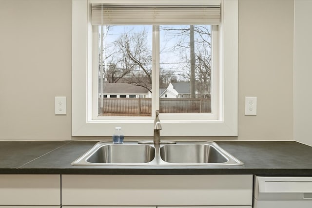 details featuring white cabinetry, dark countertops, a sink, and dishwashing machine