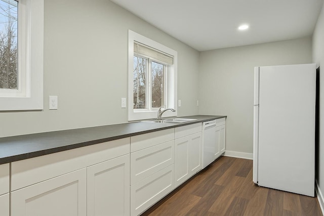 kitchen featuring a sink, dark countertops, dark wood-style flooring, and white appliances
