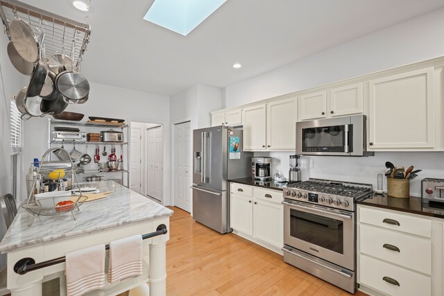 kitchen featuring appliances with stainless steel finishes, light wood-style flooring, dark stone countertops, recessed lighting, and a skylight