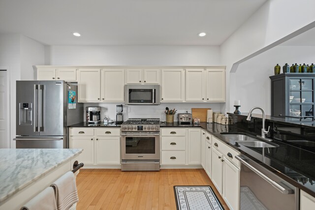 kitchen with white cabinets, appliances with stainless steel finishes, a sink, light wood-style floors, and dark stone counters